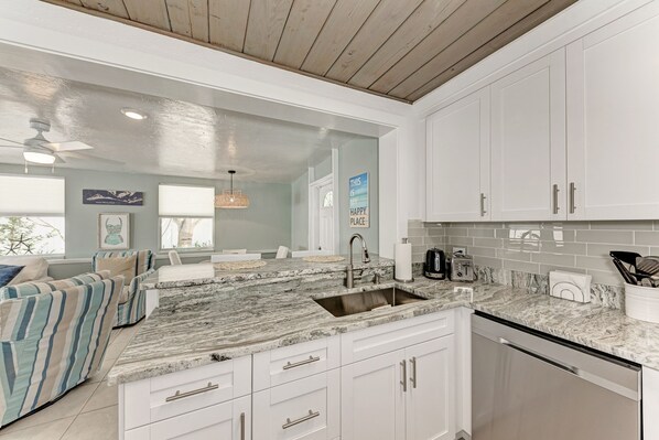 A kitchen with white cabinets, a marble countertop, and a dishwasher.