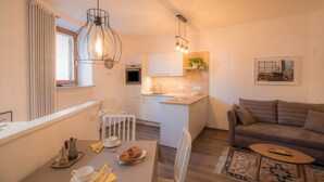 Eine moderne Küche mit weißen Schränken, ein Essbereich mit Tisch für zwei Personen und eine Wohnbereich mit Sofa und Couchtisch.