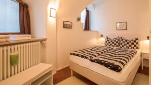 Ein Schlafzimmer mit einem Bett, einem Fenster mit Vorhängen, einem Heizkörper, einem Nachttisch und Wandbildern.