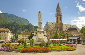 A square with a central monument, benches, and flower beds.