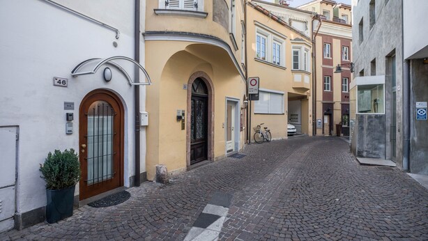 Eine Kopfsteinpflasterstraße mit Gebäuden an beiden Seiten, ein abgestelltes Fahrrad und eine Tür mit einer Nummer.