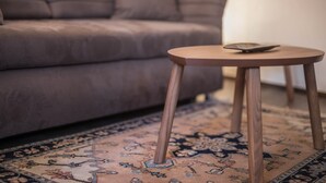 Ein runder Holztisch mit einem Smartphone darauf, vor einer Couch mit einem gemusterten Teppich.