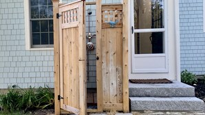 Una verja de madera con un panel decorativo, una puerta blanca y un pequeño conjunto de escalones de piedra que conducen a un porche.