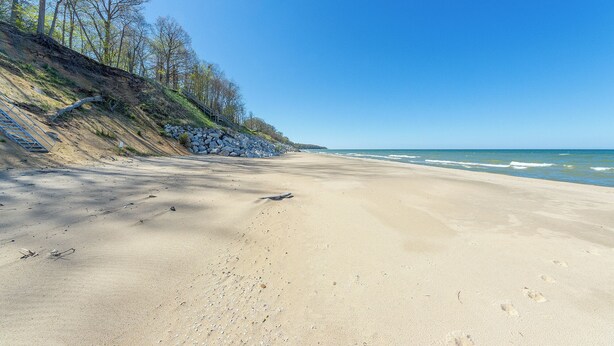 Ein Strand mit einer felsigen Klippe, blauem Himmel und Meereswellen.
