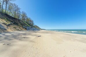 Une plage bordée d’une falaise rocheuse, sous un ciel dégagé, avec des vagues déferlant sur l’océan.