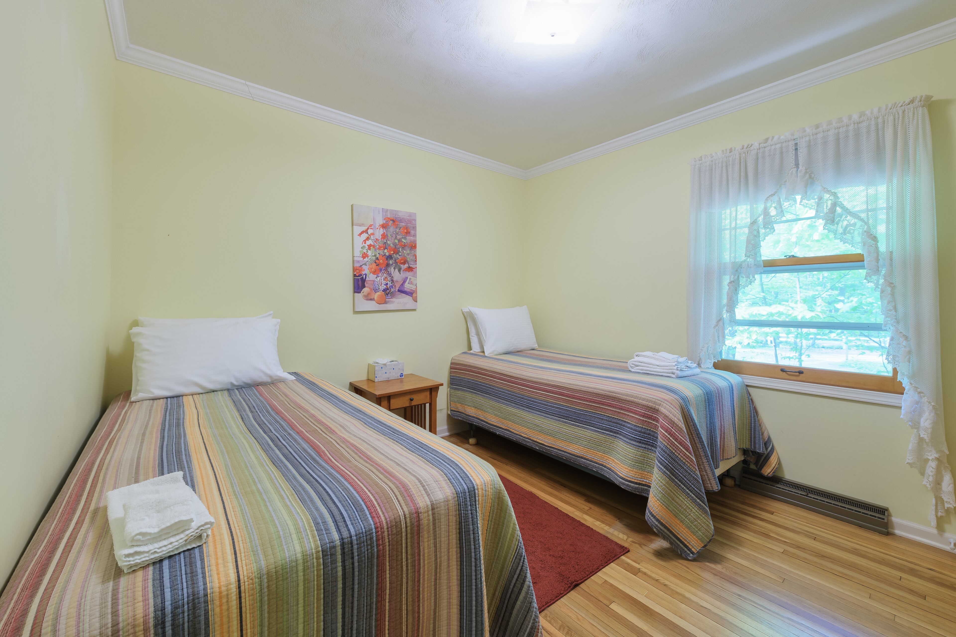 A room with two beds, a small table, and a window with curtains.