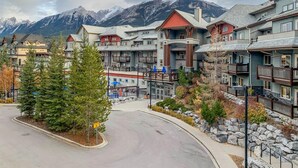 A multi-story hotel with balconies, a parking area, and a mountain backdrop. - Mountain View Penthouse 2Bdrm Loft Suite w Pool and 3 Hot Tubs (Canmore)
