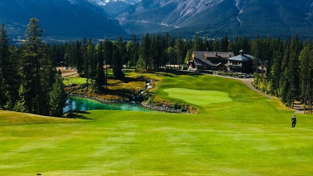A golf course with a house and mountains in the background. - Mountain View Penthouse 2Bdrm Loft Suite w Pool and 3 Hot Tubs (Canmore)
