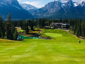 A golf course with a house and mountains in the background. - Mountain View Penthouse 2Bdrm Loft Suite w Pool and 3 Hot Tubs (Canmore)