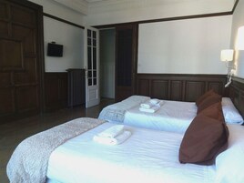 Una habitación de hotel con dos camas, un ventanal grande y una puerta que da a un pasillo.