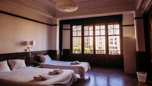 A hotel room with two beds, a large window with a view of buildings, and a chandelier. - Zentric Hostel (León)