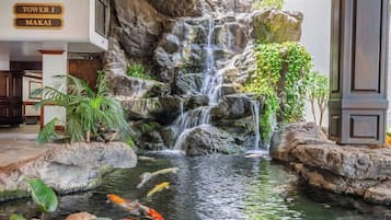 Una cascada con peces koi, rodeada de rocas y plantas, y un letrero que dice 'Tower I Makai'.