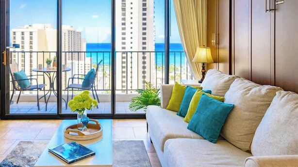 A modern living room with a sofa, a coffee table, and a view of the ocean through large windows.