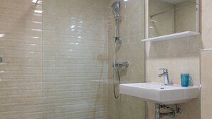 A modern bathroom with a glass-enclosed shower, a white sink with a blue cup, and a white toilet. - Apartment Navigator (Dubrovnik)