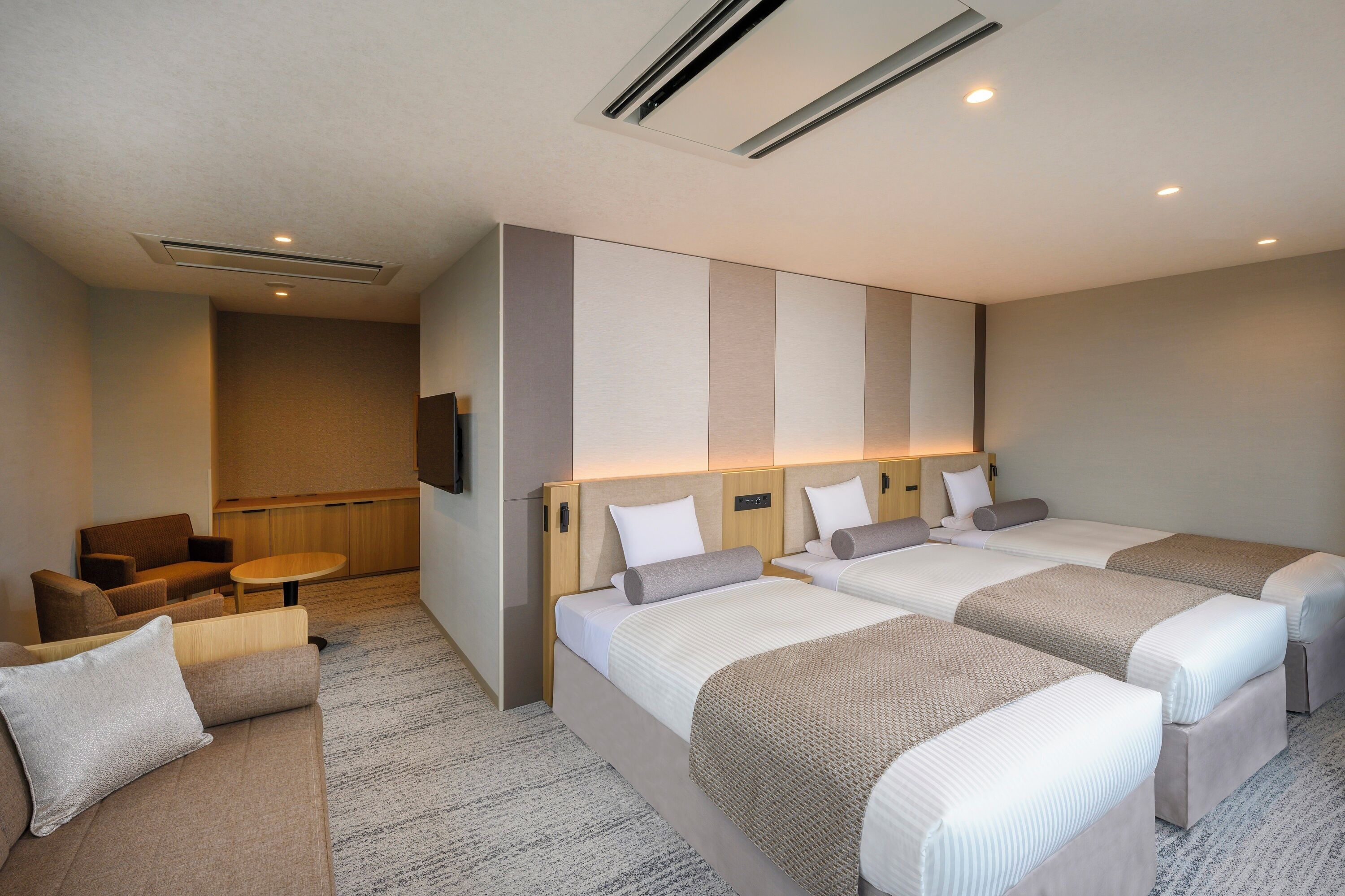 A hotel room with three beds, a sofa, a small table, and a TV.