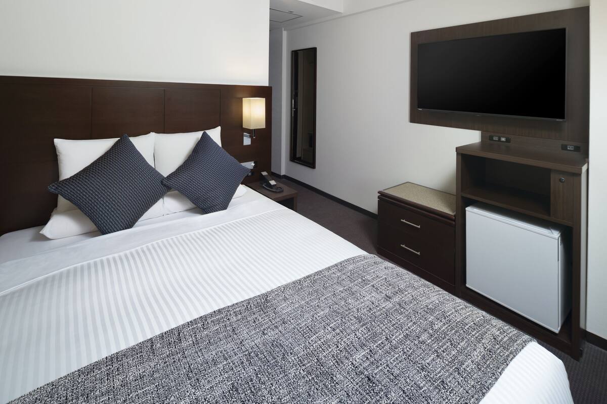 Une chambre d’hôtel avec un grand lit, un téléviseur à écran plat fixé au mur, un petit bureau avec une lampe et un miroir.