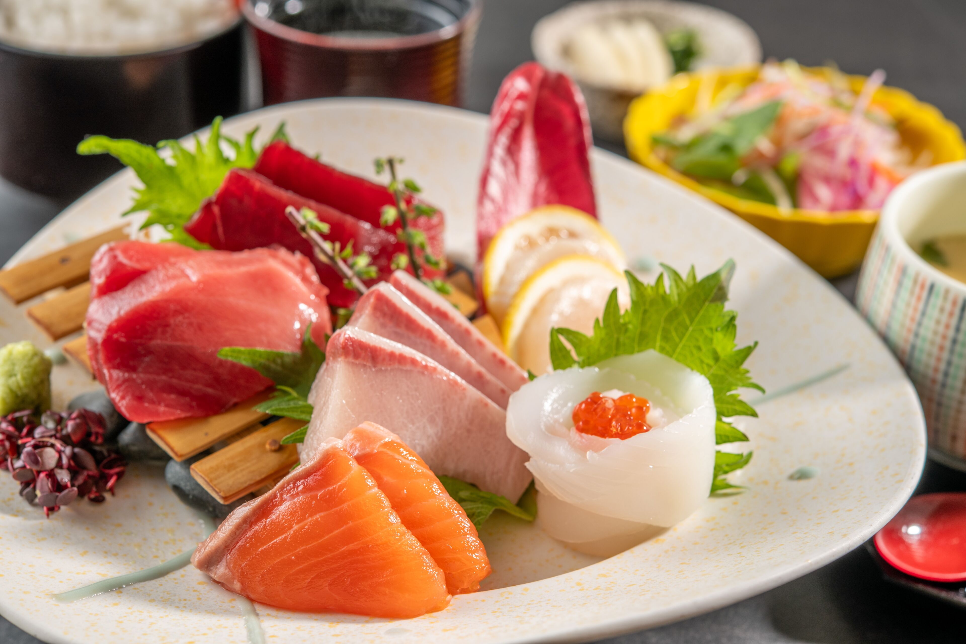 A plate of various sashimi and sushi, garnished with green leaves and lemon slices.