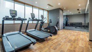 Une salle de sport équipée de tapis de course, d’un appareil elliptique et d’une zone pour les exercices de développé couché.