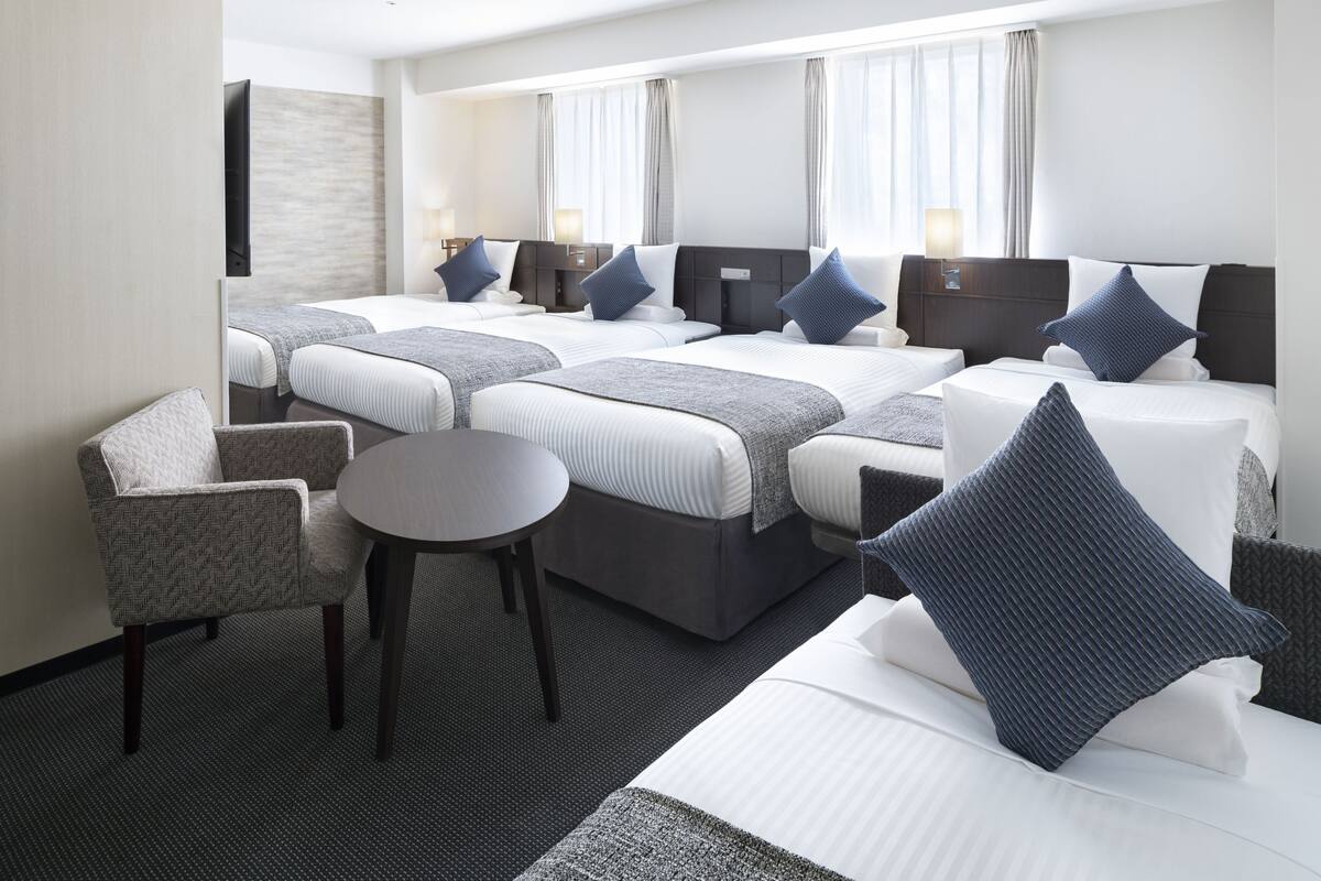 Une chambre d’hôtel avec trois lits, une petite table ronde et une chaise.