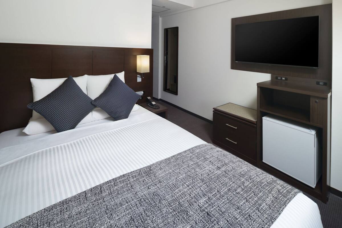 Une chambre d’hôtel équipée d’un lit, d’une table de chevet, d’une lampe, d’une télévision et d’un petit réfrigérateur.