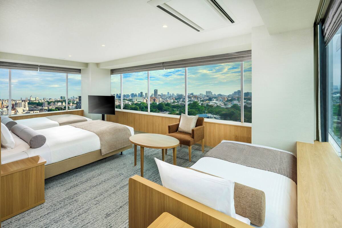 Une chambre d’hôtel moderne avec vue sur la ville, comprenant un grand lit, un canapé, une petite table et un téléviseur.