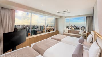 A hotel room with a large window, a flat-screen TV, two beds, a sofa, and a city view.