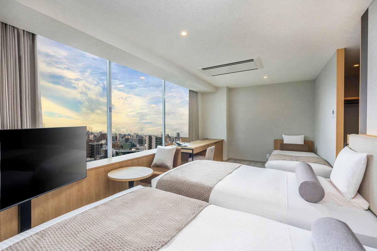 Une chambre d’hôtel moderne dotée d’une grande fenêtre, d’un téléviseur à écran plat, d’un bureau et de deux lits.