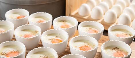 A series of white ramekins with a cooked egg in each, a wooden cutting board, a bowl of yellow liquid, and a carton of eggs.