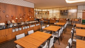 Un restaurant avec des tables et des chaises en bois, un buffet proposant divers plats et, au fond, un espace cuisine.