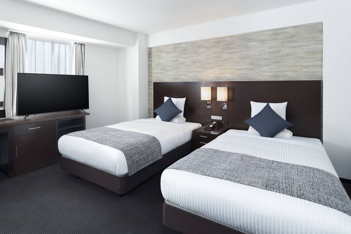 Une chambre d’hôtel avec deux lits, une télévision, un bureau et une table de chevet.