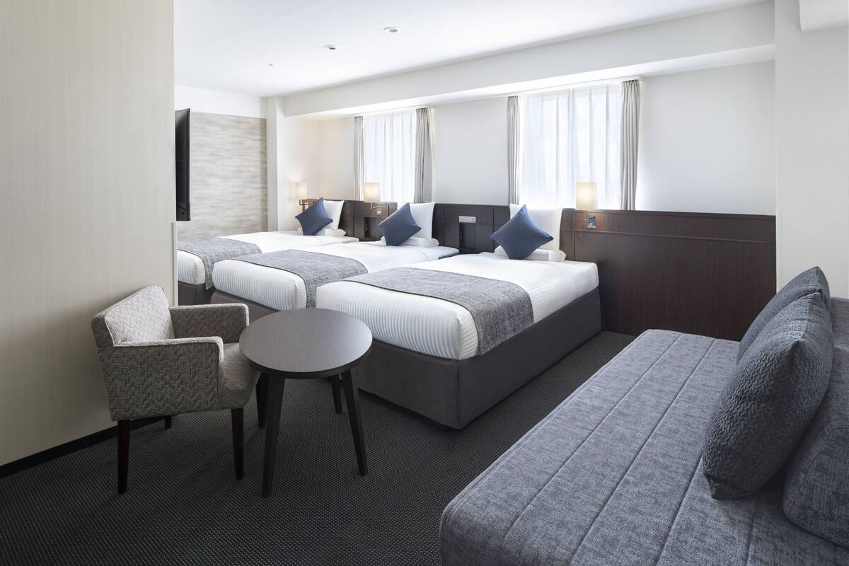 Une chambre d’hôtel avec deux lits, un canapé, une chaise et une petite table.