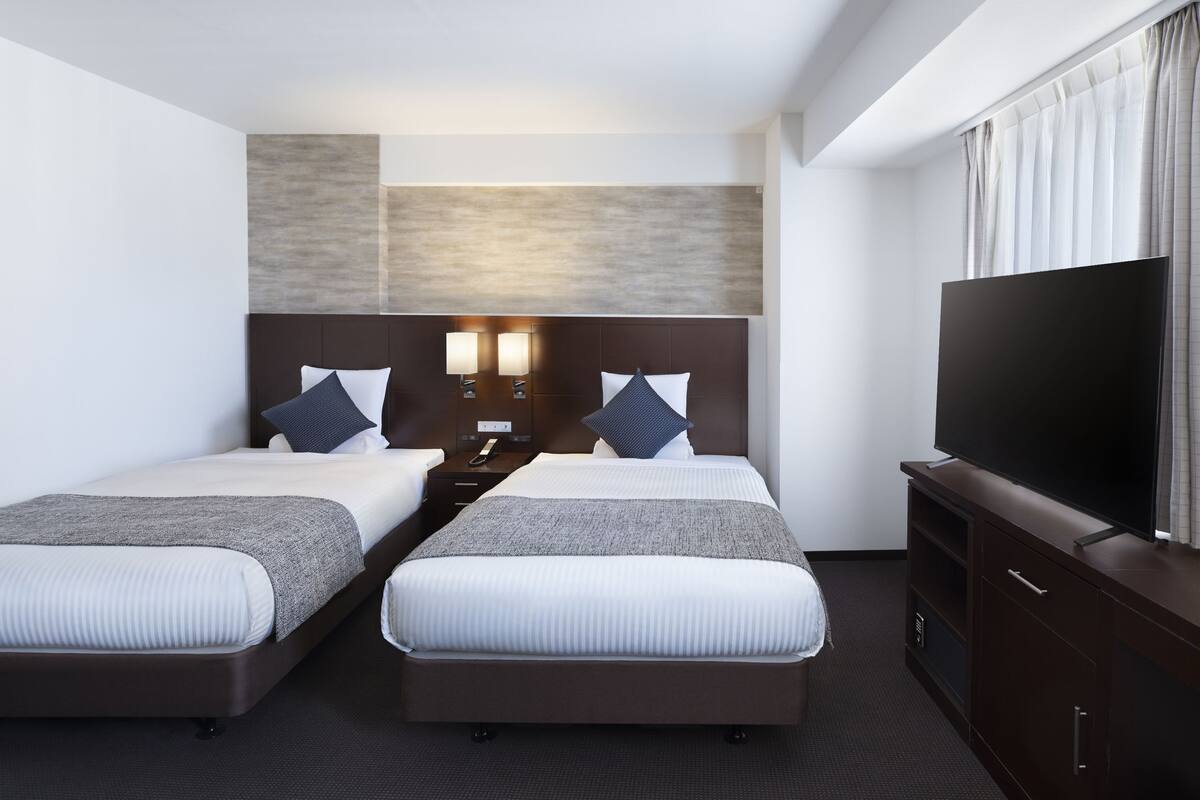 Une chambre d’hôtel avec deux lits, un téléviseur à écran plat et une table de chevet avec une lampe.