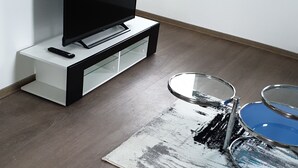 A modern living room with a flat-screen TV on a black and white entertainment unit, a glass coffee table, and a patterned rug. - Air-conditioned apartment 2, great connection to Vienna + super-fast WLAN (Neulengbach)