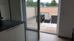 A modern kitchen with a sliding glass door leading to an outdoor patio with wicker furniture and a wooden deck. - Air-conditioned apartment 2, great connection to Vienna + super-fast WLAN (Neulengbach)