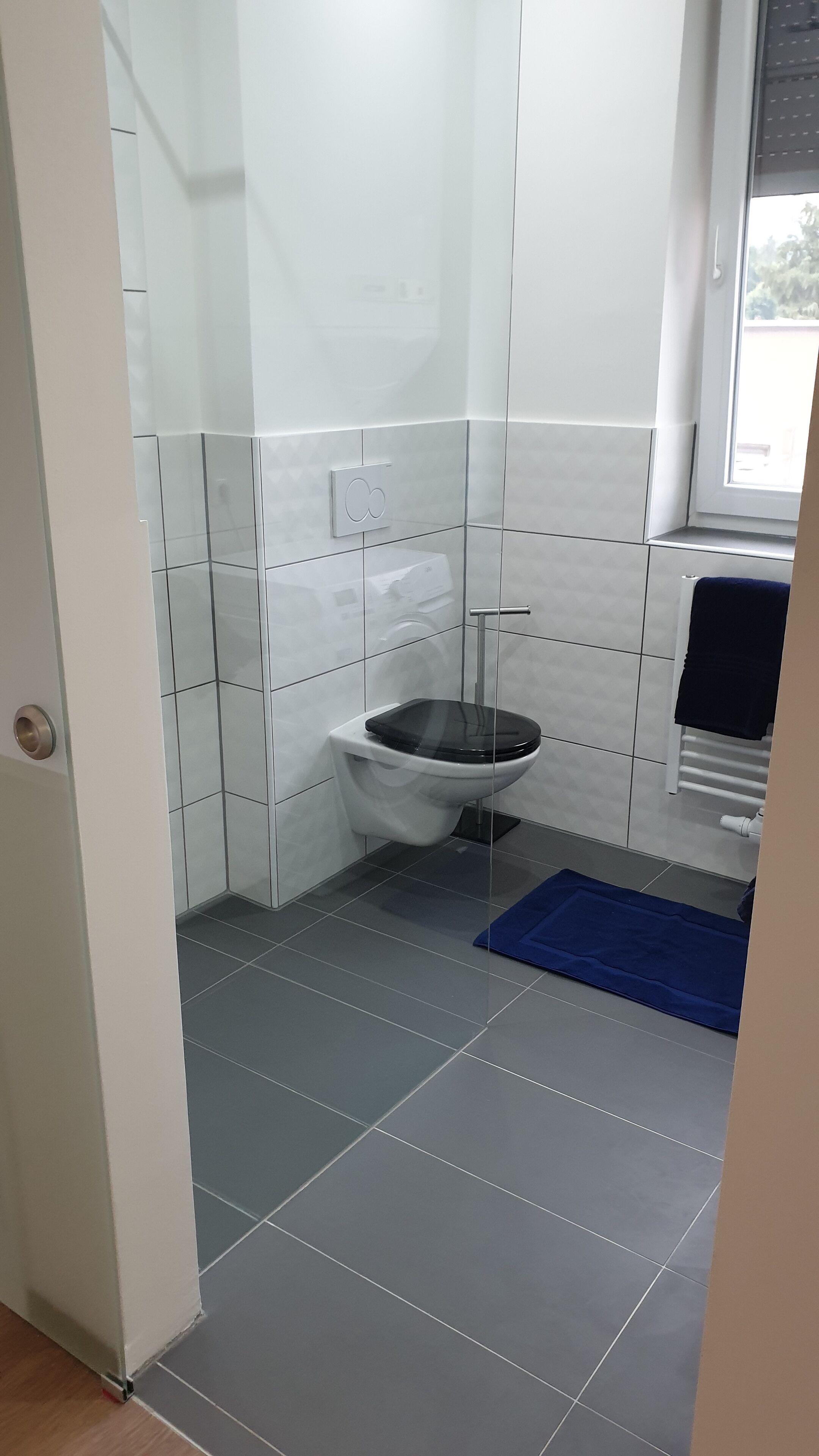 A small bathroom with a toilet, a towel rack, and a window.