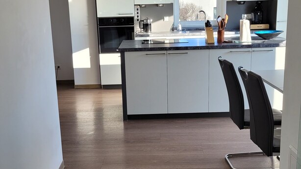 A modern kitchen with white cabinetry, a central island, and a view of a residential area. - Air-conditioned apartment 2, great connection to Vienna + super-fast WLAN (Neulengbach)