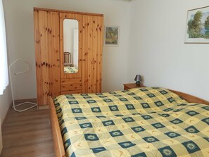 Ein Schlafzimmer mit einem Bett, einem Holzschrank, einem Spiegel, einem kleinen Tisch mit Lampe und einem gerahmten Bild an der Wand.