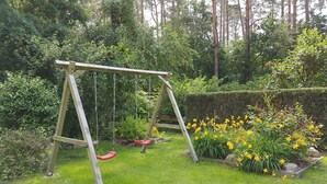 A wooden swing set in a lush garden with green grass and yellow flowers. - Lenz Süd Fw 1 - Holiday apartment 1 - 68027 (Fünfseen)