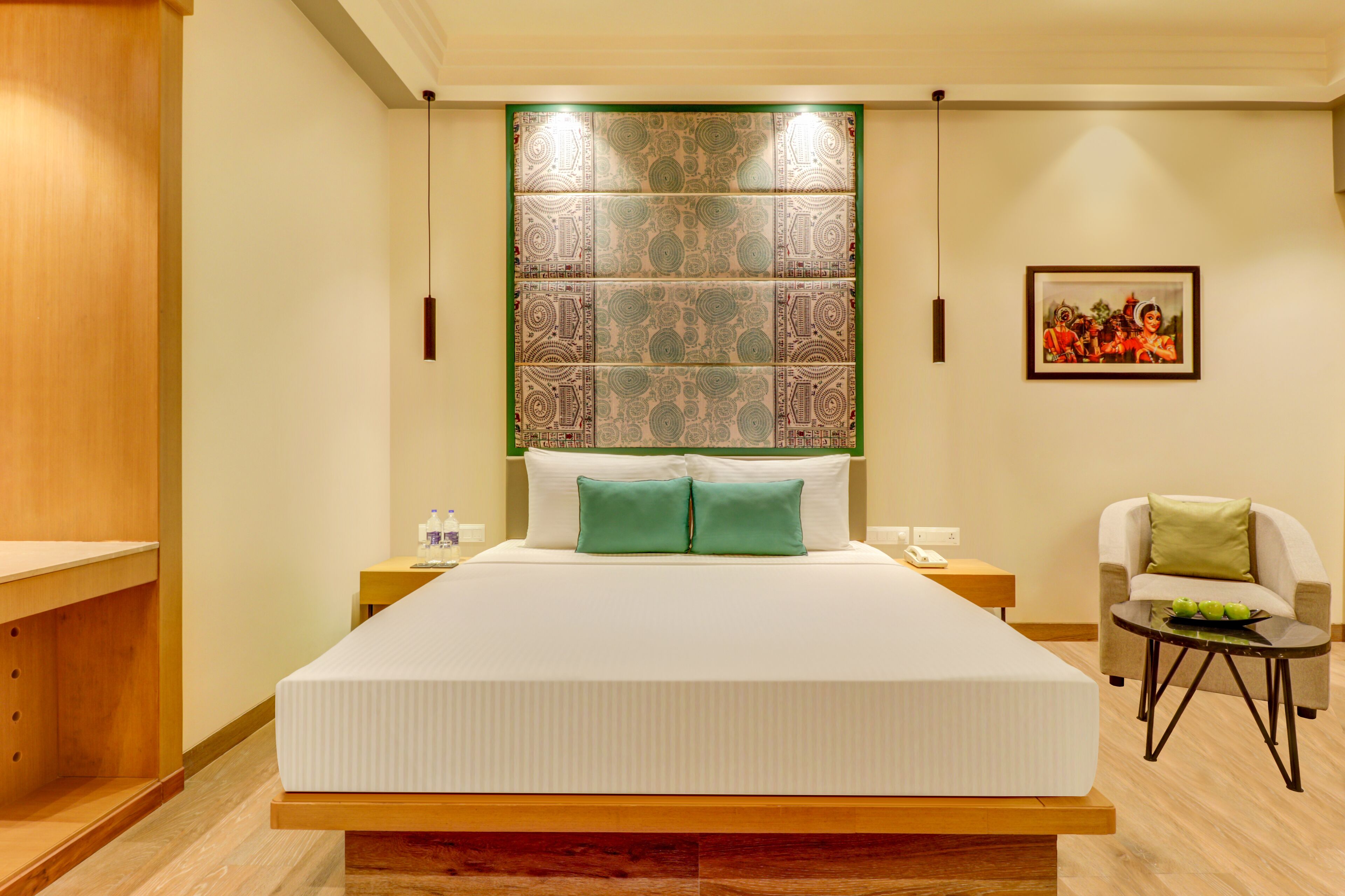 Habitación de hotel con una cama grande, una mesita con un tazón verde, una silla y una obra de arte colgada en la pared.