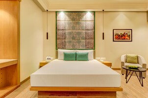 Habitación de hotel con una cama grande, una mesita con un tazón verde, una silla y una obra de arte colgada en la pared.