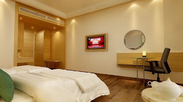 A hotel room with a bed, a TV displaying news, a round mirror, a table with a chair, and a teapot.