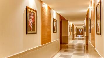 A hotel hallway with framed artwork on the walls, a checkered floor, and a wooden panel accent.