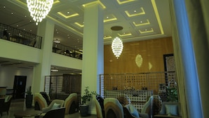 Un hall d’entrée avec un plafond haut, des lustres, un espace salon et un mur en bois orné d’un motif décoratif.