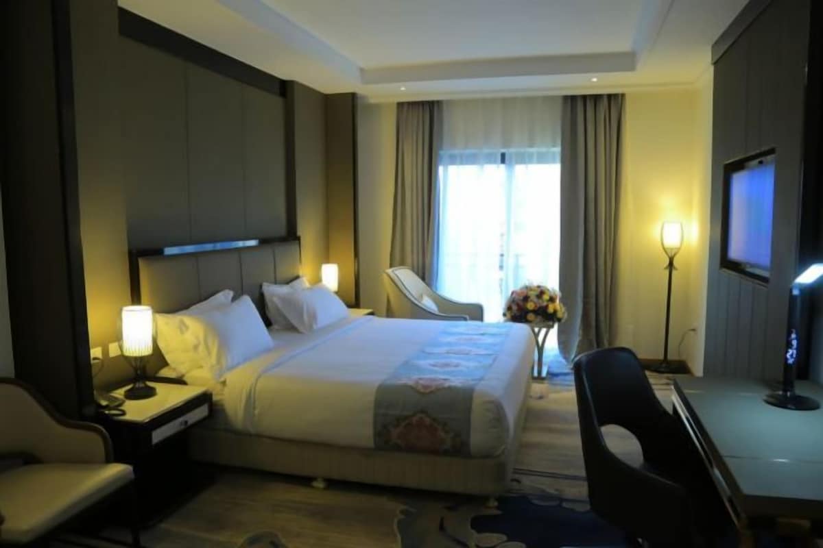 A hotel room with a bed, a desk, a chair, a TV, and a window with curtains.