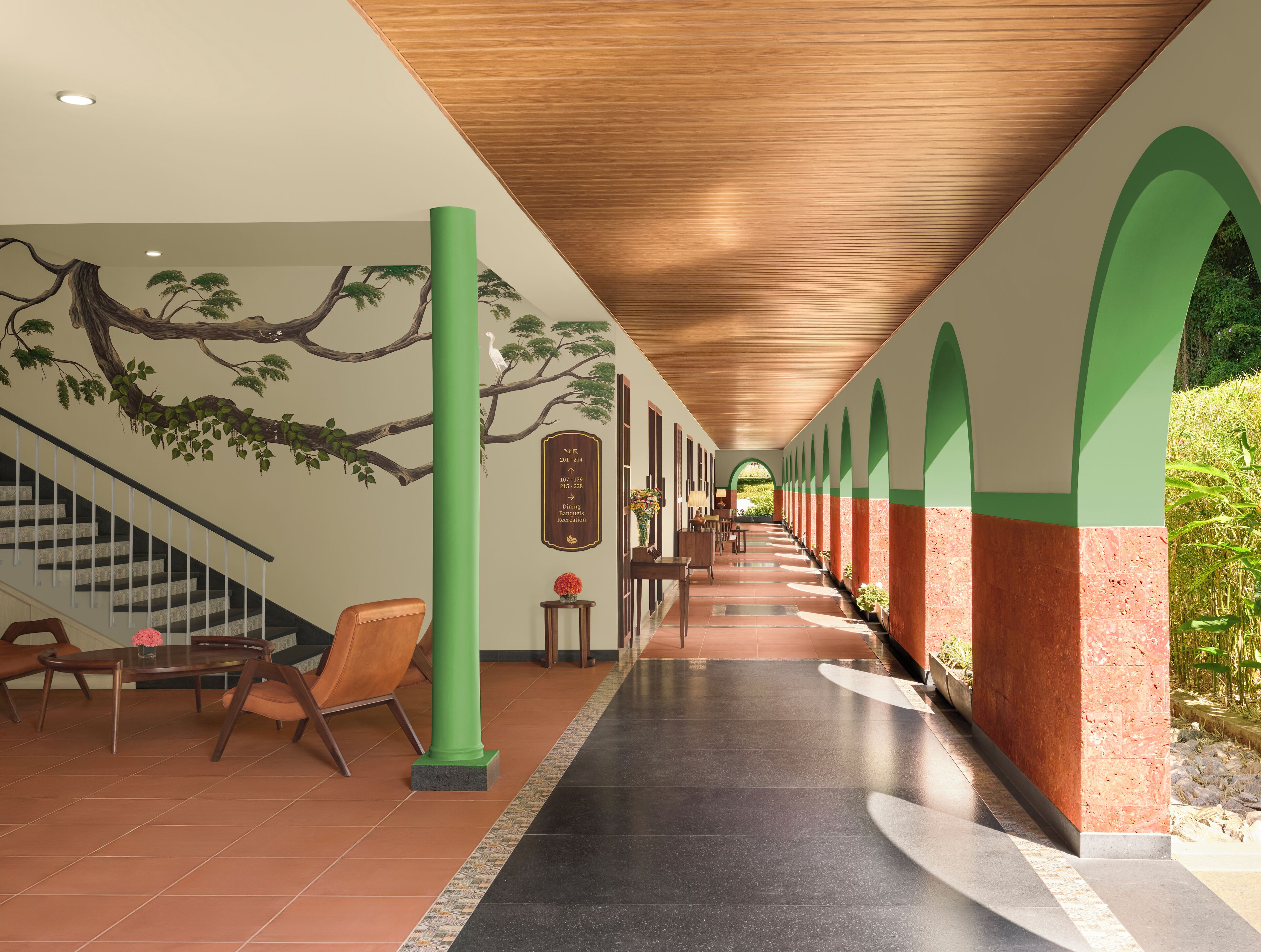 A corridor with a wooden ceiling, tiled flooring, and green and red walls. There are chairs and a table with a vase of flowers.