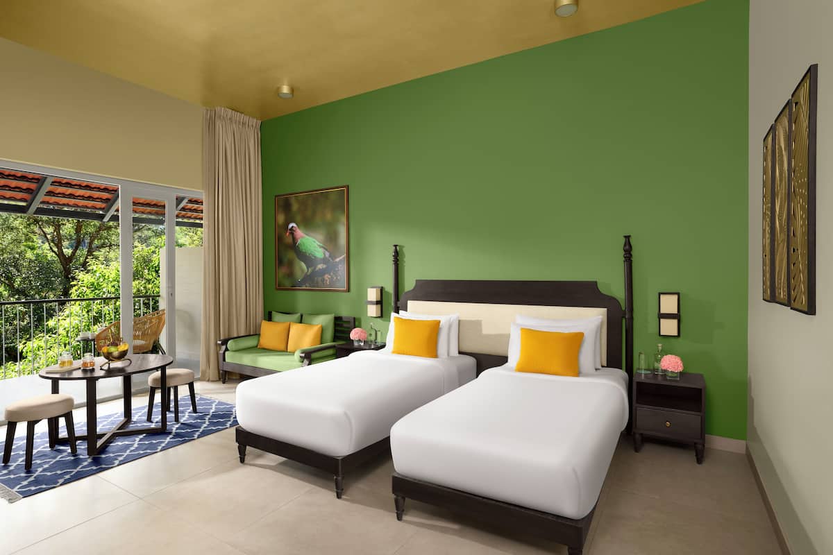 A hotel room with two beds, a dining table, and a balcony with a view of greenery.