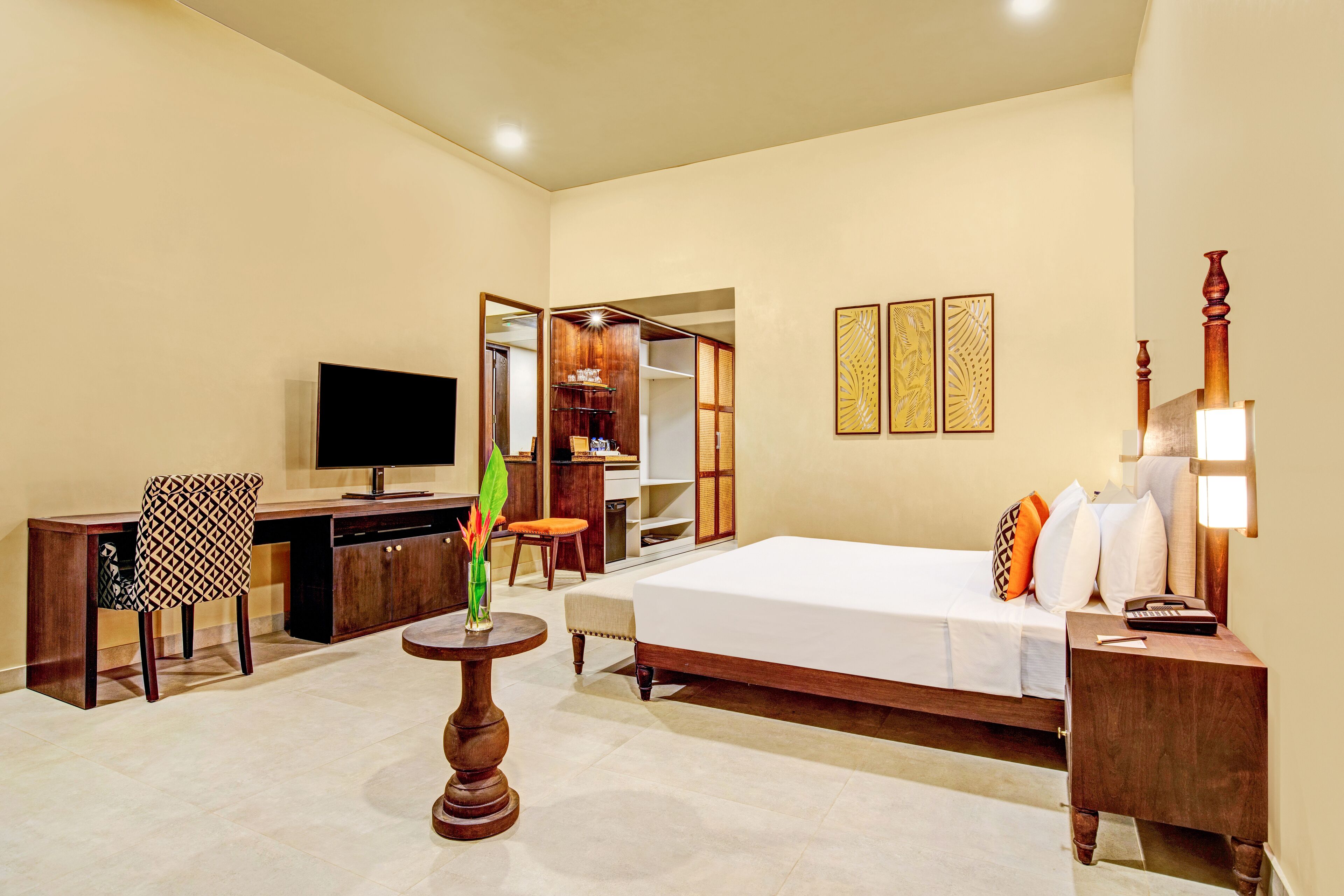 A hotel room with a bed, desk, chair, TV, and a small table with a plant.