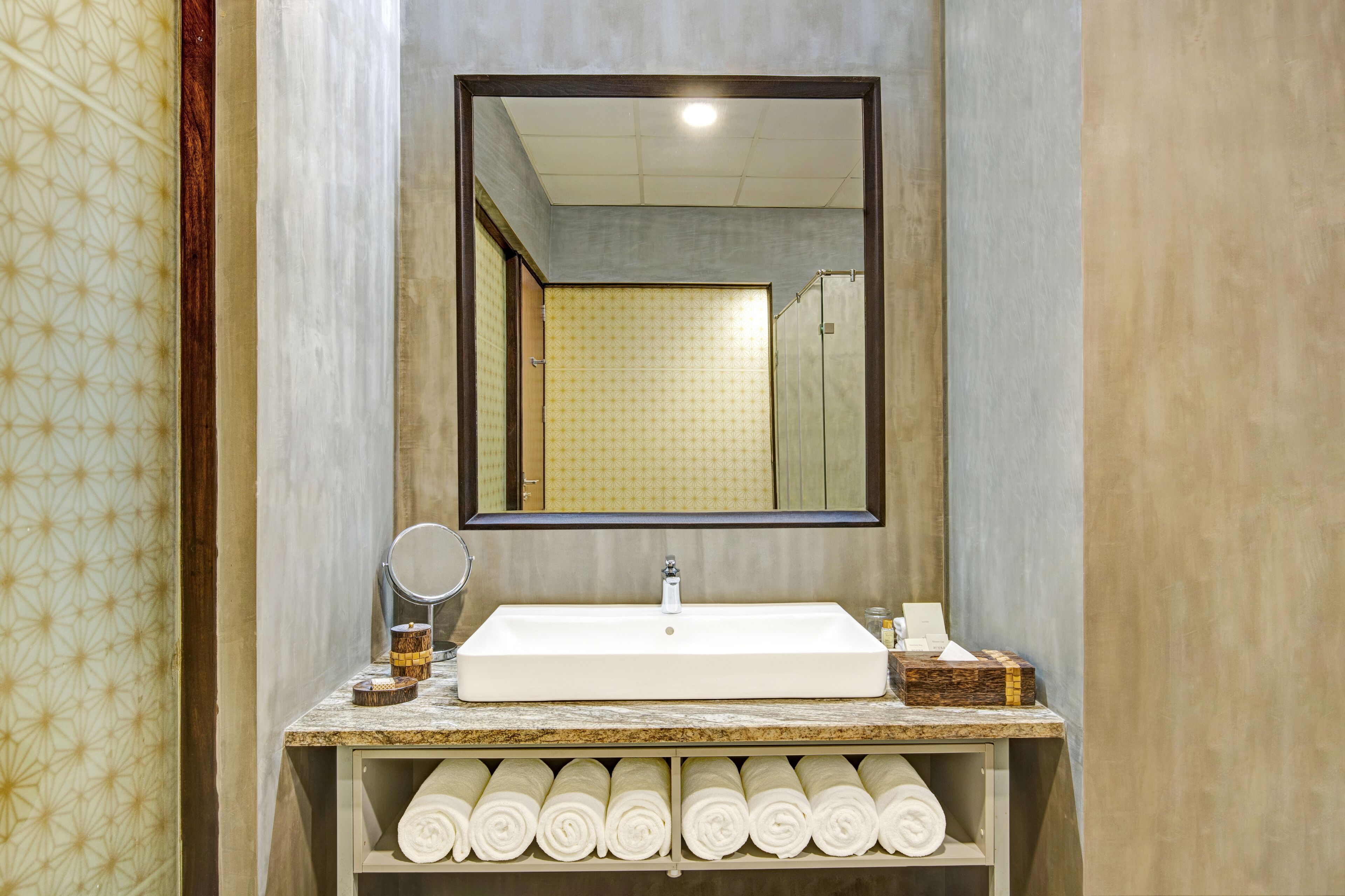 Un baño con un espejo grande, un lavabo blanco y una estantería con toallas ordenadamente dobladas.