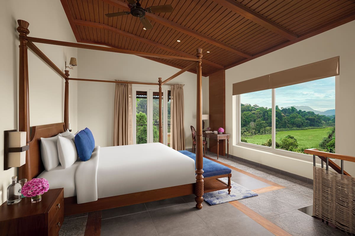 A four-poster bed with a view of a lush landscape through large windows.