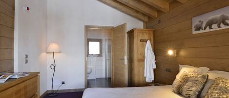 A bedroom with a wooden ceiling, a bed with white bedding, a wooden dresser, a lamp, and a polar bear painting on the wall.